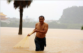 暴雨致水位上涨民众雨中网鱼